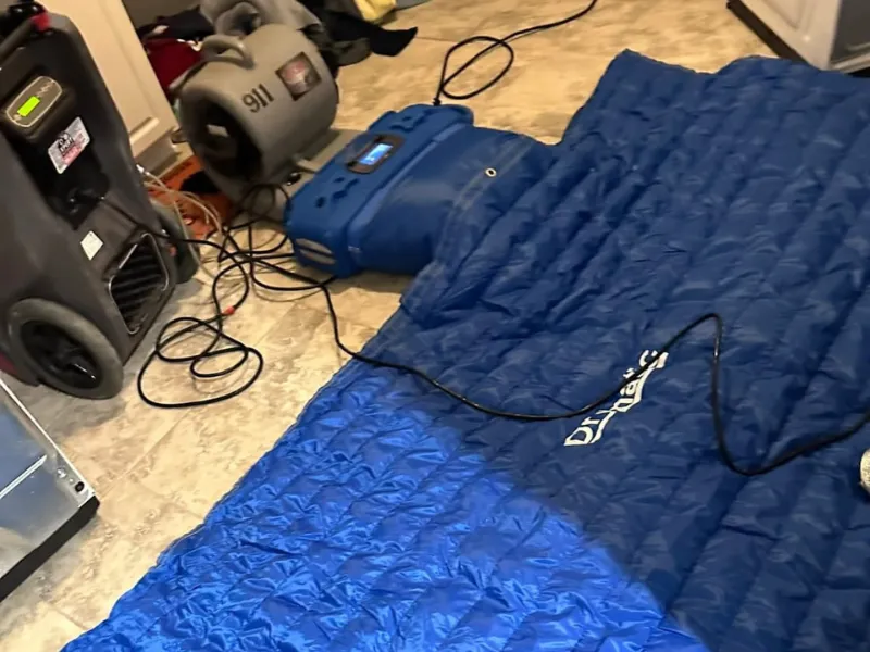 Blue drying mat connected to air movers on a tiled floor.