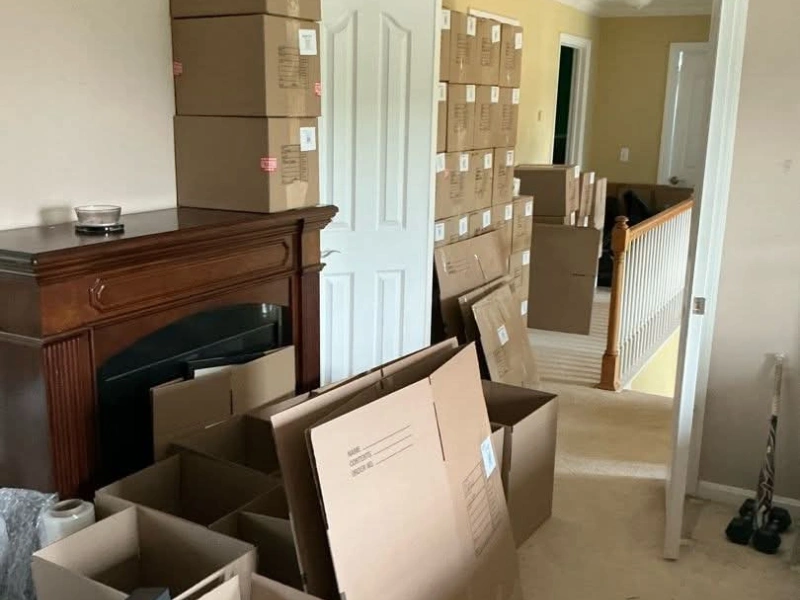 Stacks of packed cardboard boxes filling a hallway and room near a wooden fireplace.