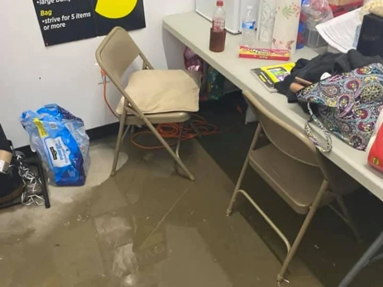 Flooded room with two folding chairs, a table cluttered with items, and water covering the floor.