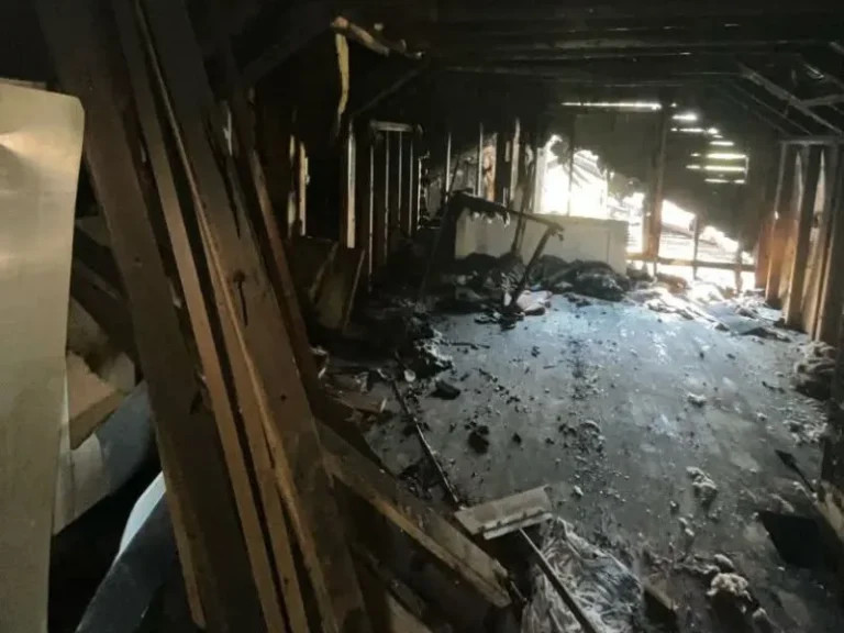 Interior of a damaged attic with exposed beams and debris scattered on the floor.