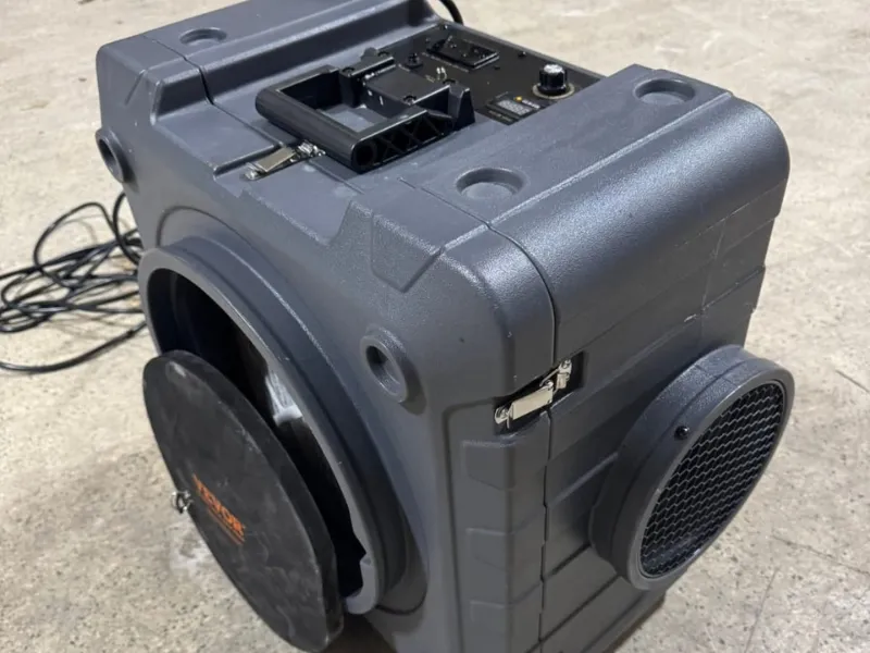 Portable gray speaker with a handle, control panel, and a round black grille on the side.