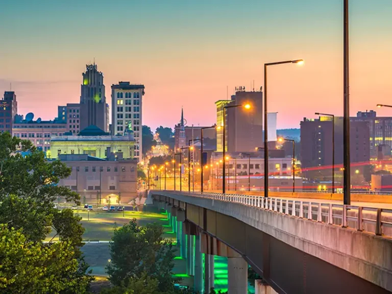 City skyline at dusk with a lit bridge extending into the distance.